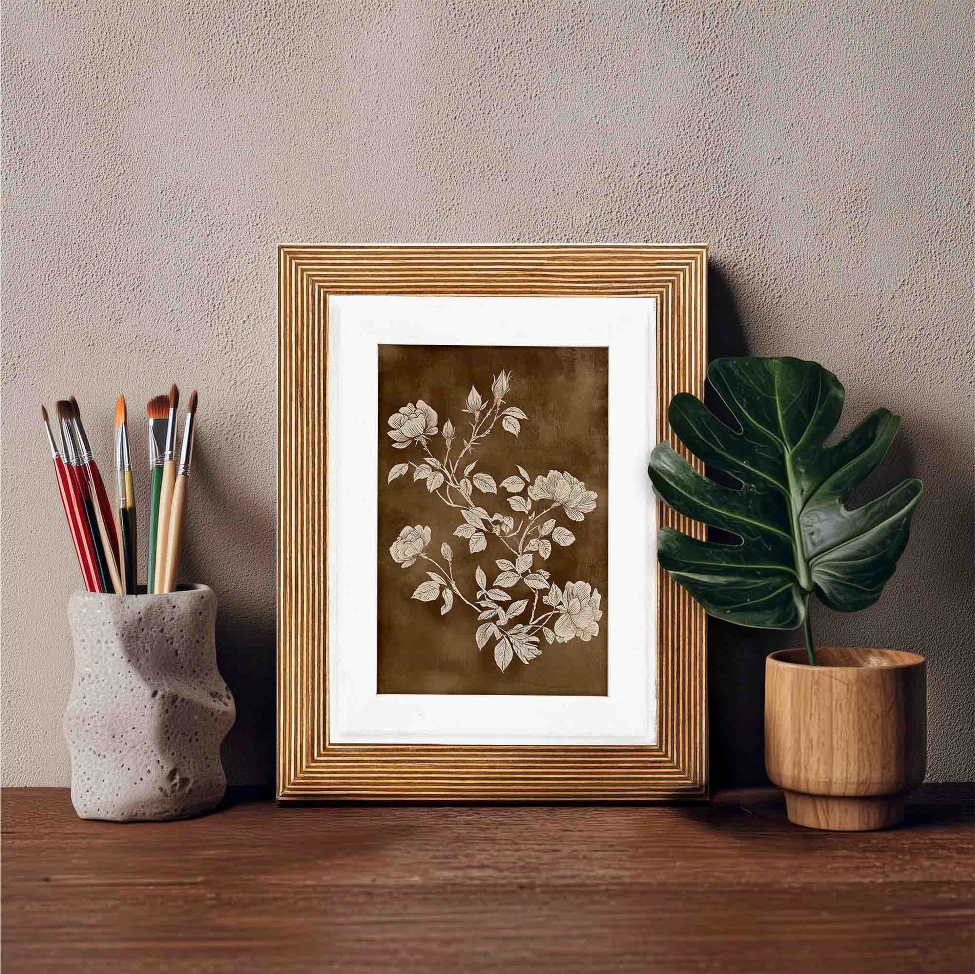 Botanical print framed in an natural wooden picture frame on a wooden shelf with art supplies and a plant.