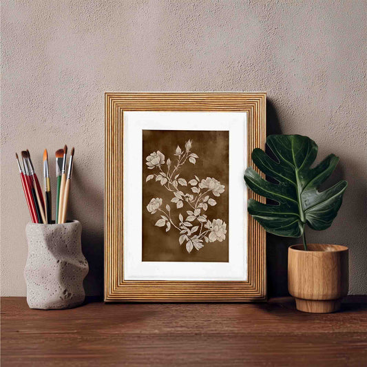 Botanical print framed in an natural wooden picture frame on a wooden shelf with art supplies and a plant.
