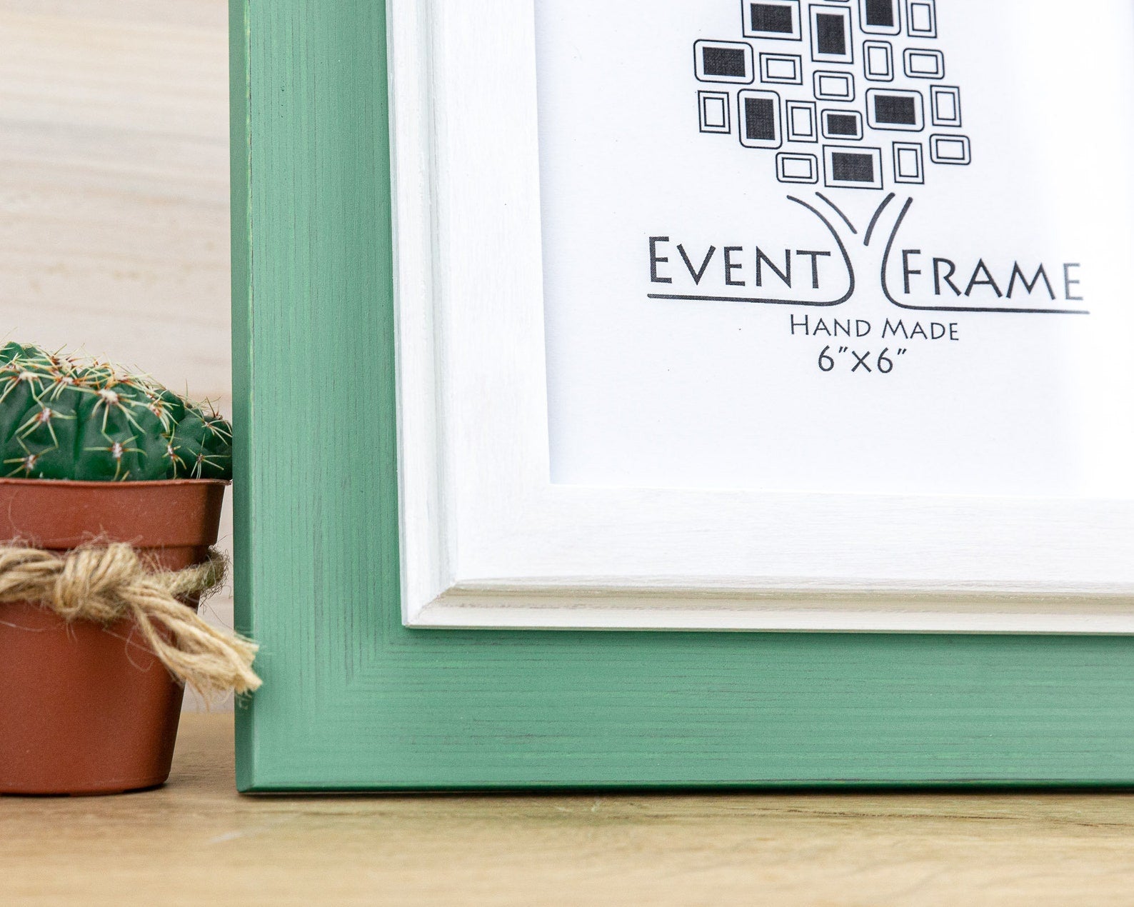 Green picture frame with 'Event Frame' logo on a wooden surface next to a small potted cactus. Grey and white rustic birch frame with handmade charm and clean contrast. Eco-finished and perfect for art, photos, or calm modern wall décor.