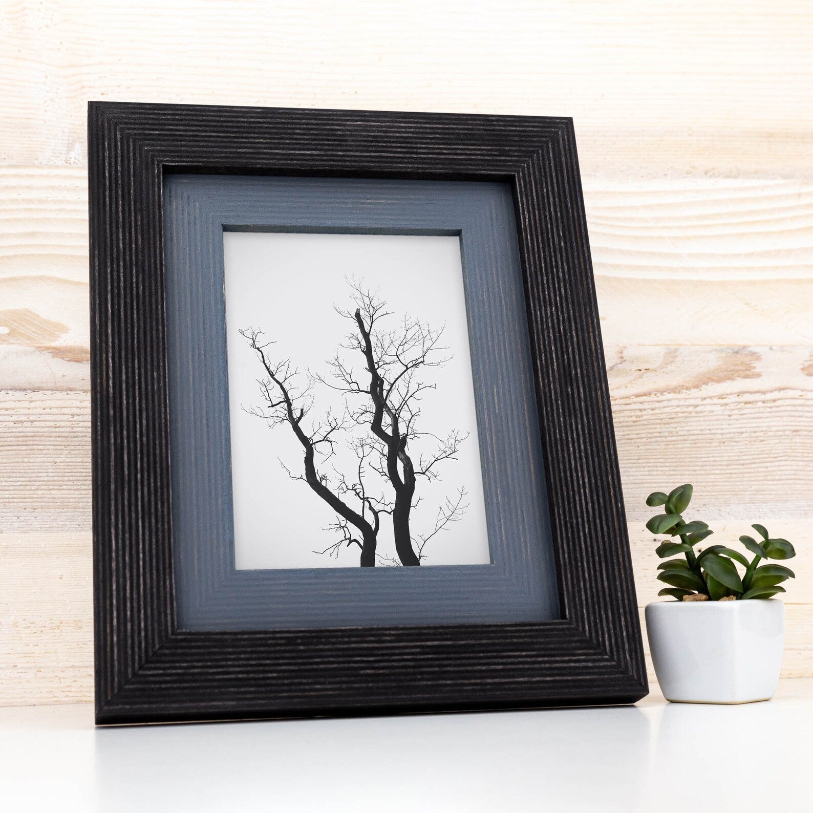 Framed black and white tree print on a wooden surface with a small potted plant.Black + Grey Handmade Picture Frame, Photo Frame with Wooden Mat, Two Tone Poster Wall Frame, Custom Sizes A1 A2 5x7 8x10 18x24 24x36 20x30
