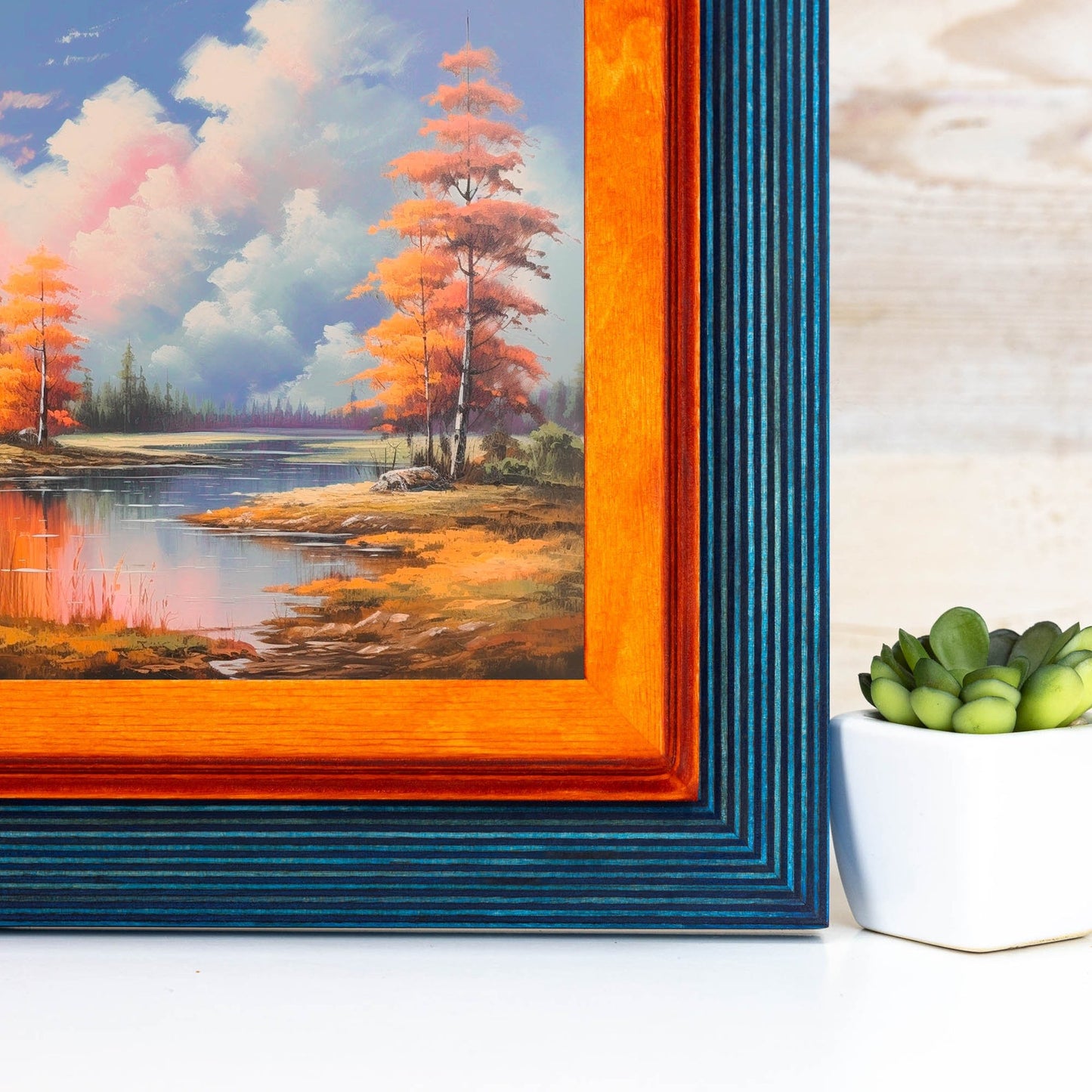 Framed painting of a landscape with trees and water, next to a potted plant on a wooden surface. Add rustic elegance with this grey + white birch frame. Handmade and built to last, ideal for artwork, photo décor, or Scandi-inspired homes.
