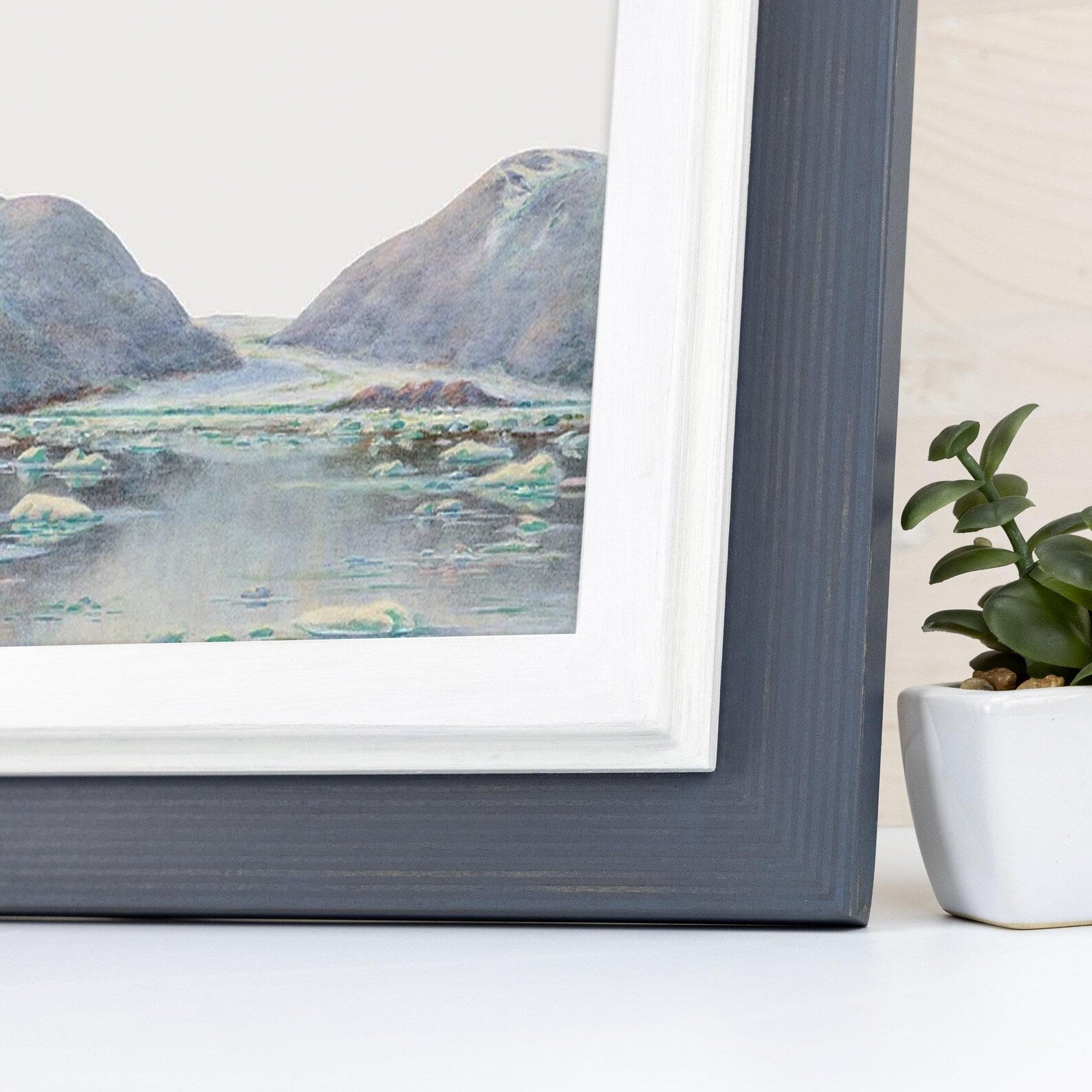 Framed artwork of a landscape with mountains and water, next to a potted plant.Charcoal Grey + White Custom Size Frames, Double Color Frame for Poster, Handmade Wooden Photo Frame, Cold Tones A2 A3 11x14 22x22 36x42