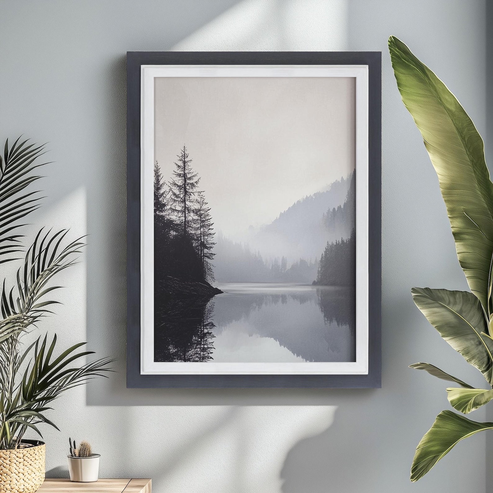 Framed artwork of a misty landscape with trees and water, placed on a wall with plants around. Charcoal Grey + White Custom Size Frames, Double Color Frame for Poster, Handmade Wooden Photo Frame, Cold Tones A2 A3 11x14 22x22 36x42