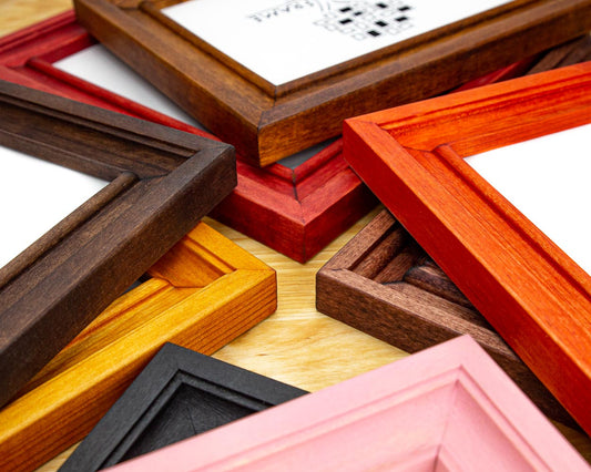 A collection of various solid birch hardwood picture frames in different colors including white, black, brown, red, and pink, with visible wood grain patterns.