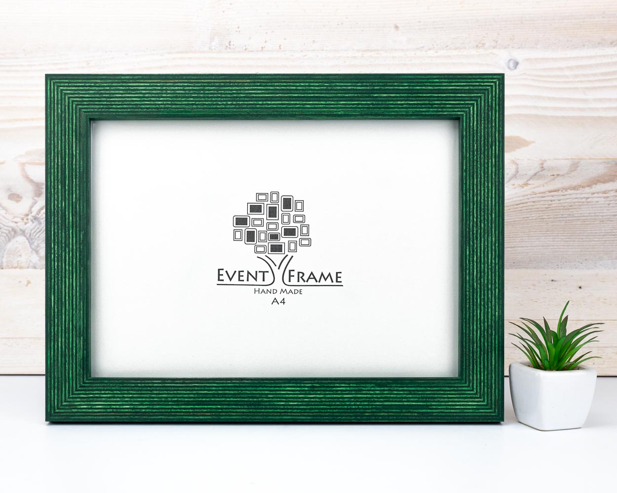 A green solid birch hardwood picture frame with a unique stripy design, displayed on a white background alongside a small potted plant.