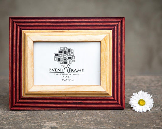 A rustic design picture frame with a red exterior and natural wood interior, displayed with a white artwork piece and a small flower beside it.