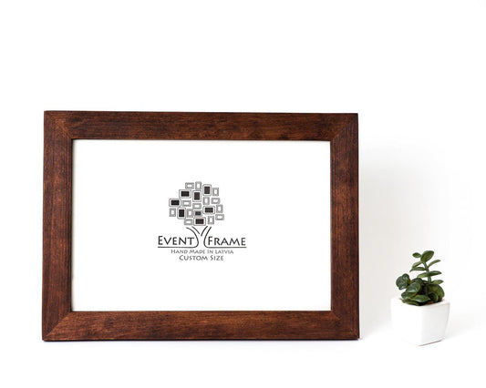 A brown modern design photo frame made from solid birch hardwood, displayed with a custom photo insert of EventFrame, standing upright with a white background and a small potted plant to the side. Custom wooden picture frame, birch hardwood, brown walnut color, handmade quality, custom sizes A4, A5, A3, 8x10, 5x7, 20x30, 14x18, 22x28