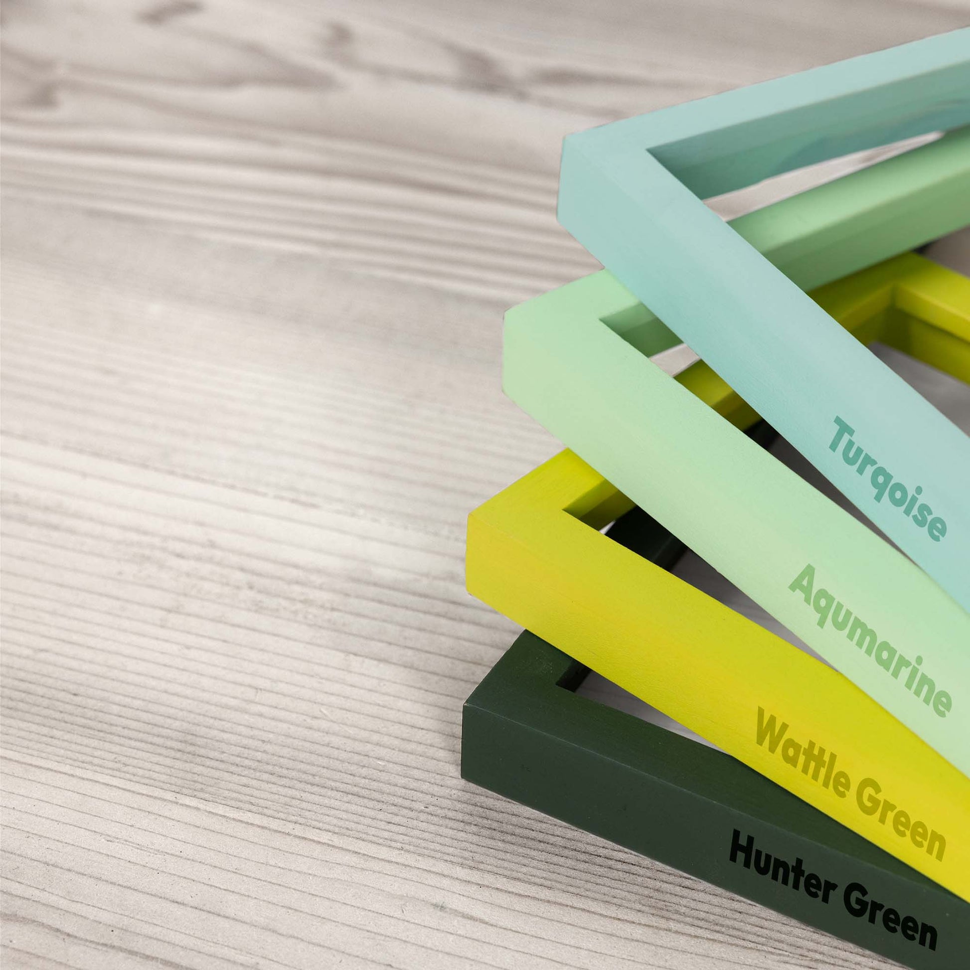 Stack of colorful photo picture frames labeled with green shades on a textured surface, frames in turquoise, aquamarine, wattle green and hunter green colors. 