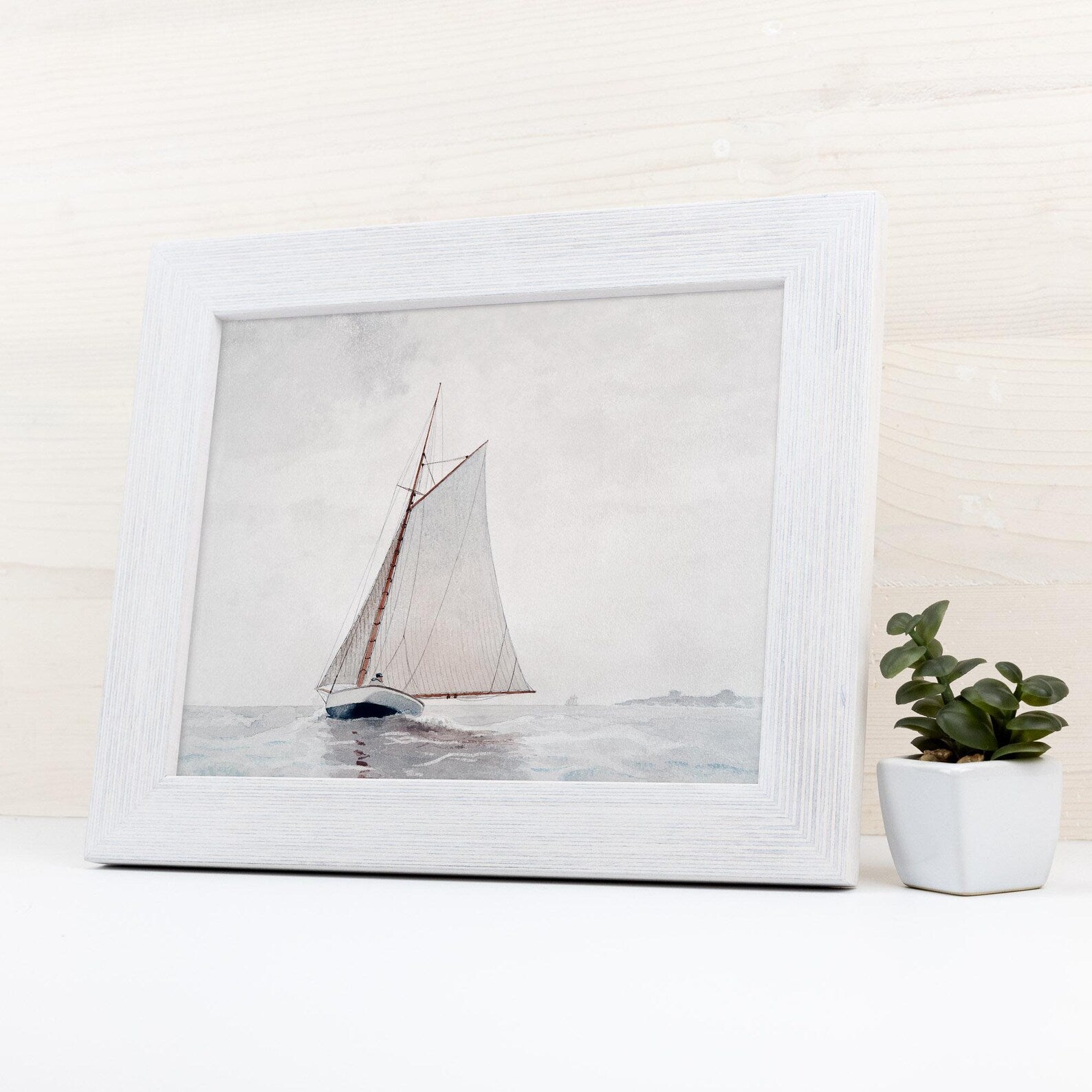 Framed artwork of a sailboat on water with a plant beside it
