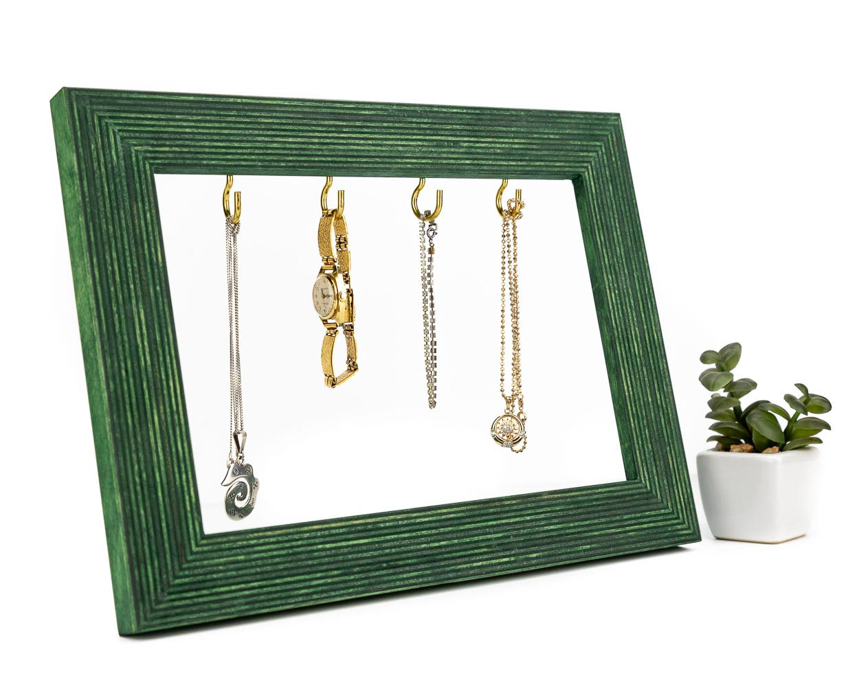 Green wooden frame holding jewelry with a green plant next to it.